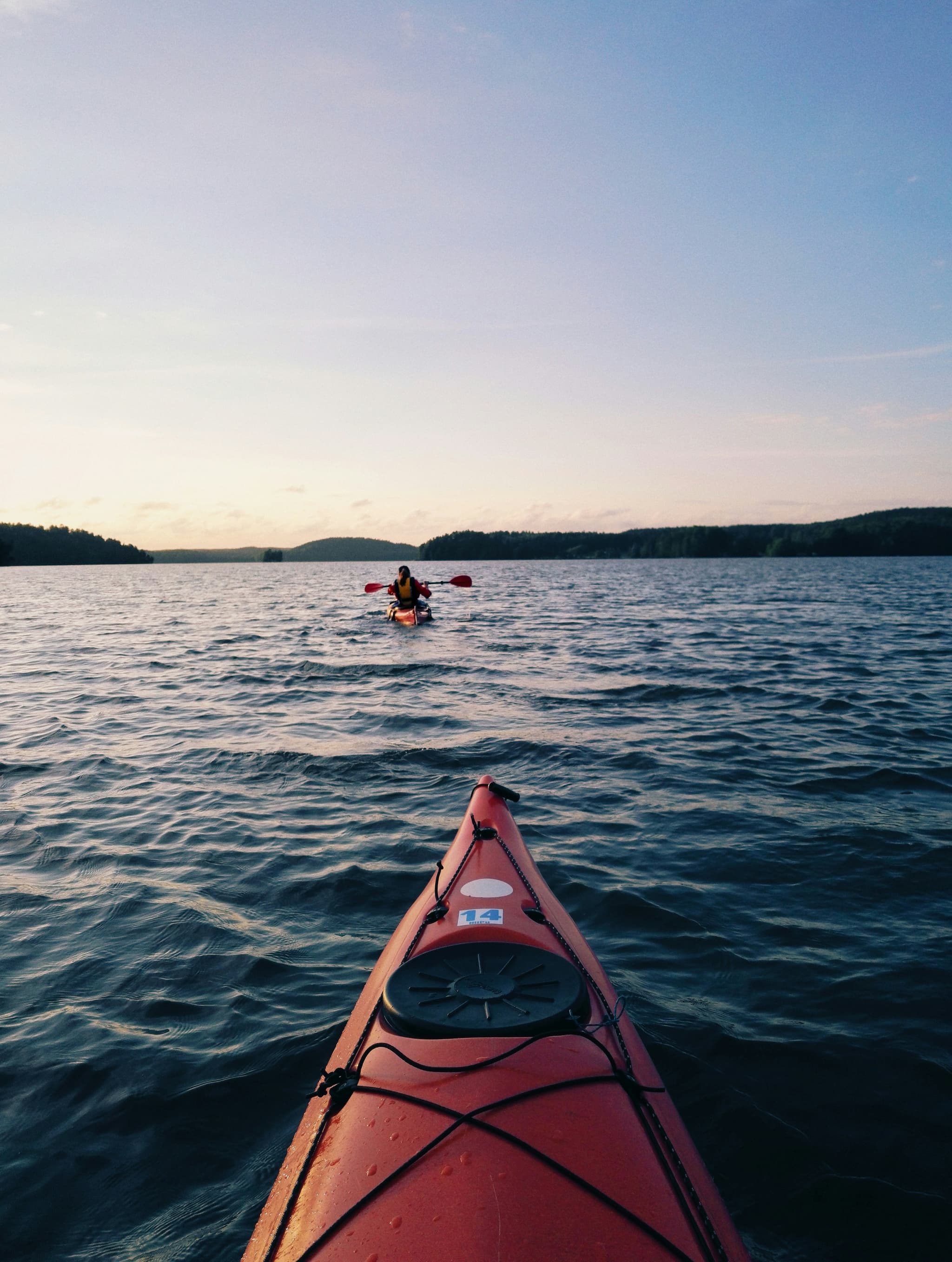 Kayaker on Lake With Forested Shoreline Kayaker in a red kayak paddling on a calm lake with forested hills in the background.