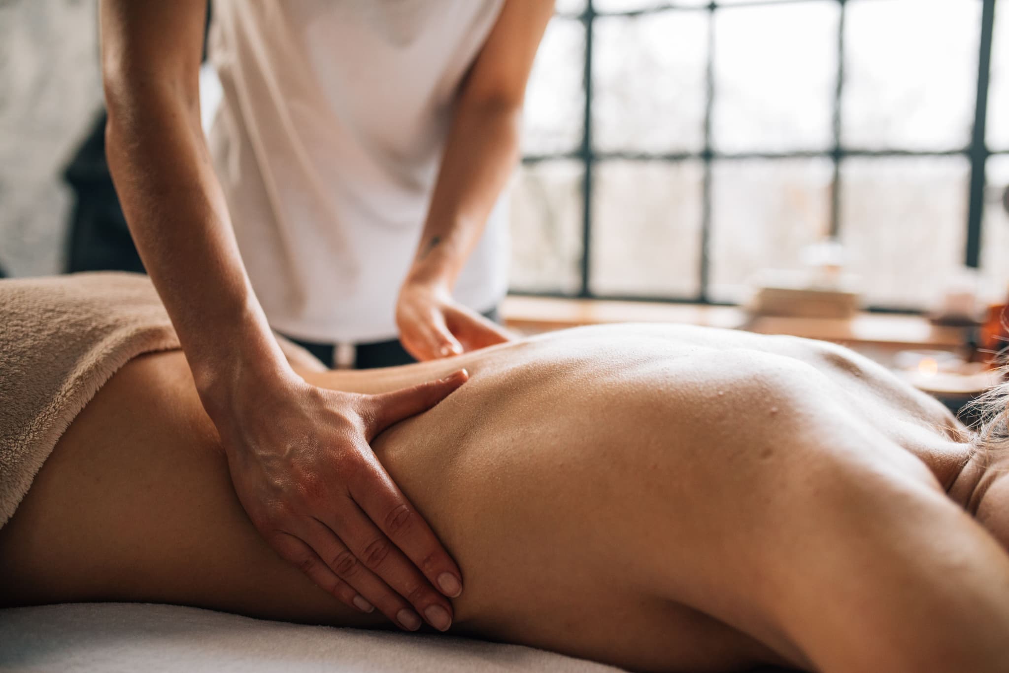Therapeutic Leg Massage in Studio Massage therapist applying pressure to a client's leg during a therapeutic massage session in a bright studio with large windows.