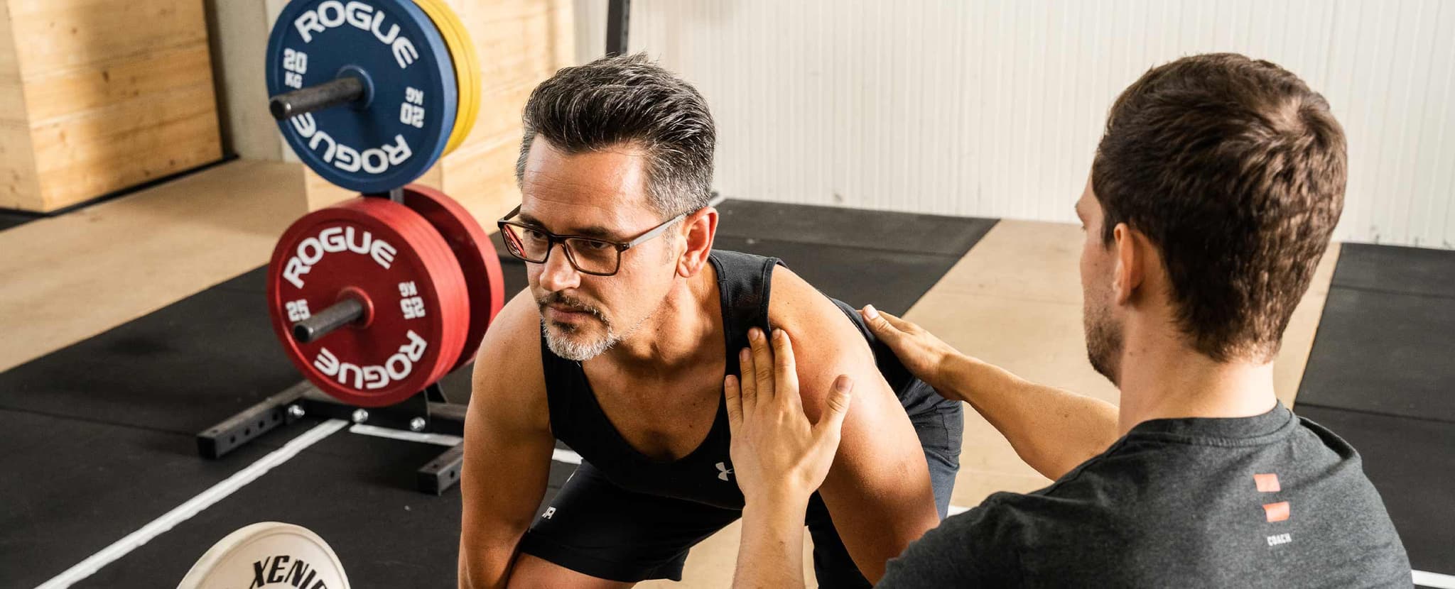 Trainer coaches clients at the gym Trainer corrects a man's shoulder position during a workout at the gym.