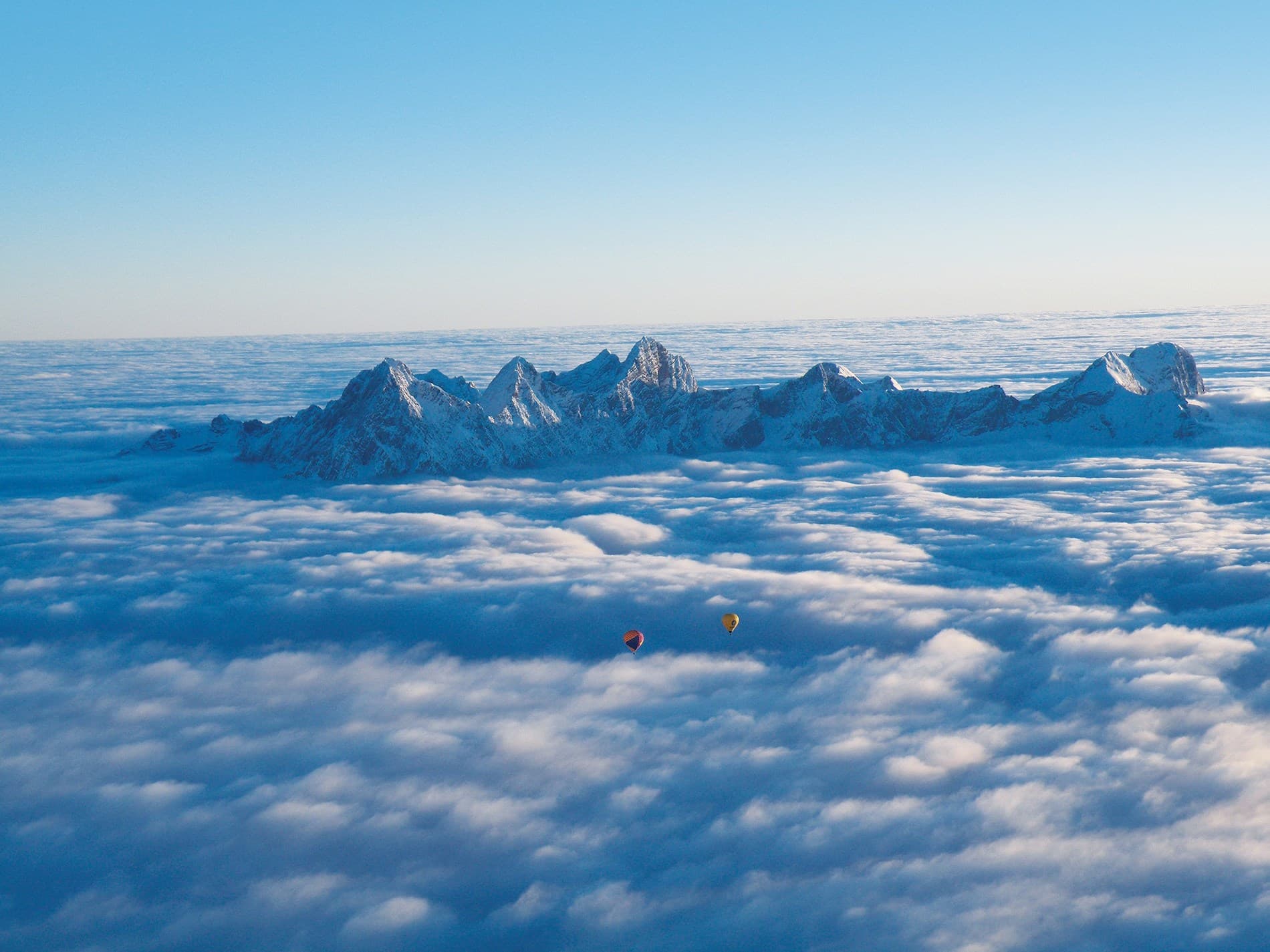Hot Air Balloons Above Cloud Sea Two hot air balloons floating above clouds near snowy mountain peaks.