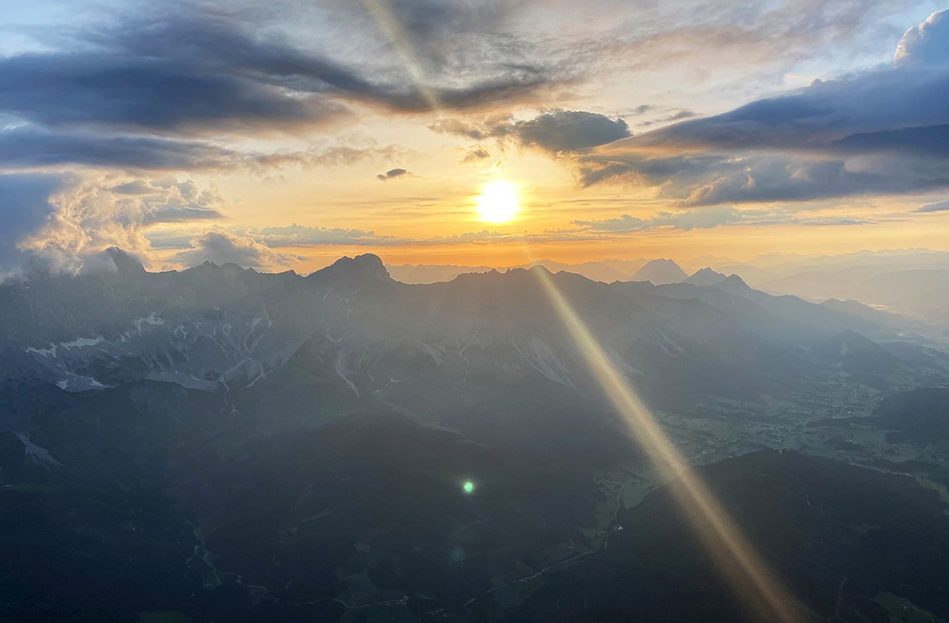Sunset Over Mountain Range Aerial view of sun setting over mountain peaks with clouds and sunbeam.
