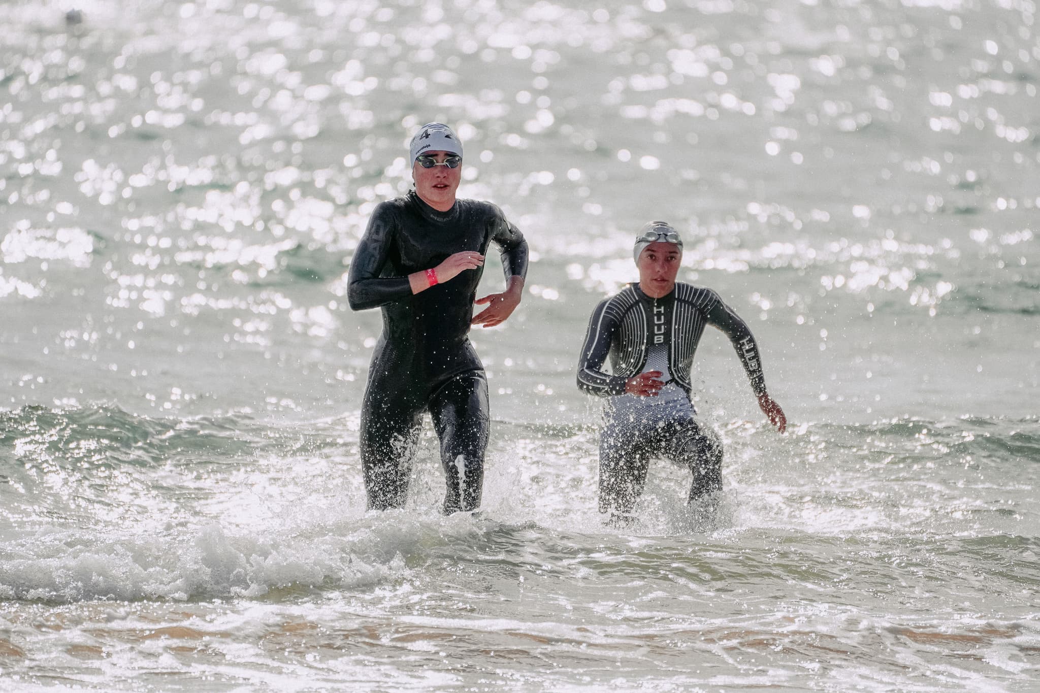 Open Water Swimmers Entering the Ocean Two open-water swimmers in wetsuits and swim caps running into ocean waves during a race.
