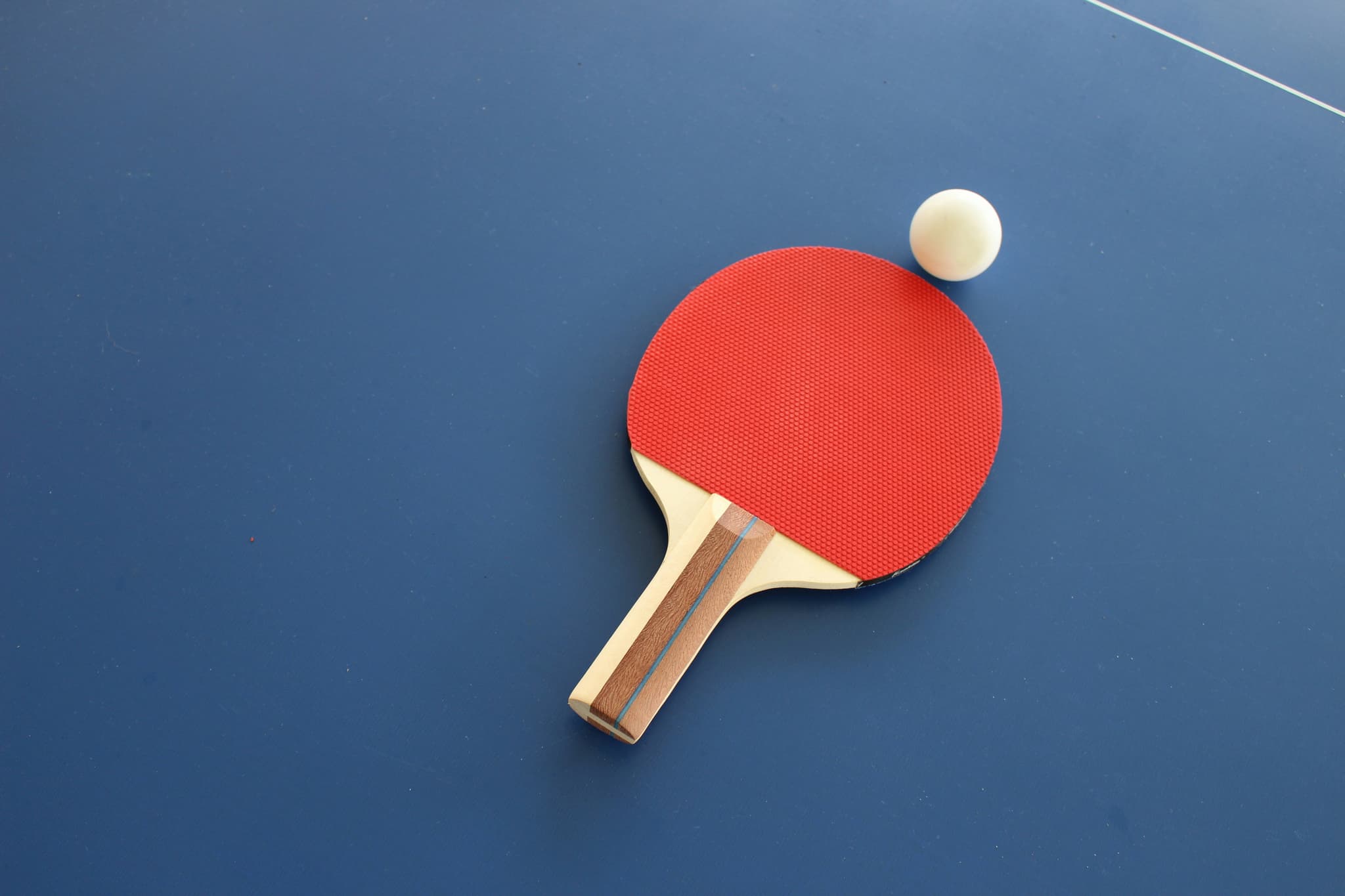 Ping Pong Paddle and Ball Red ping pong paddle with wooden handle and white ball on blue table.