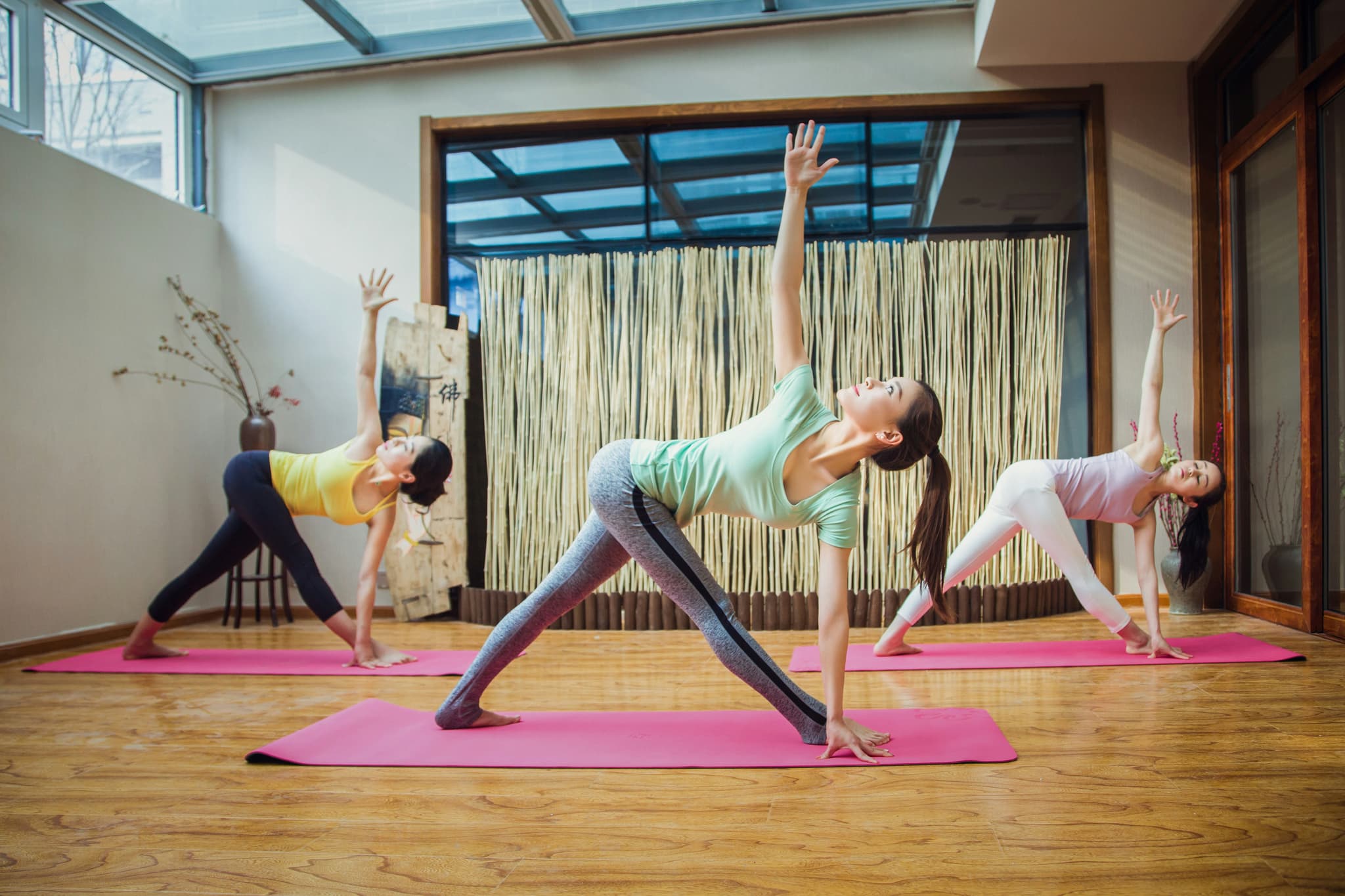 Yoga Class in a Bright Studio Three women practice triangle pose on pink mats in a bright yoga studio.