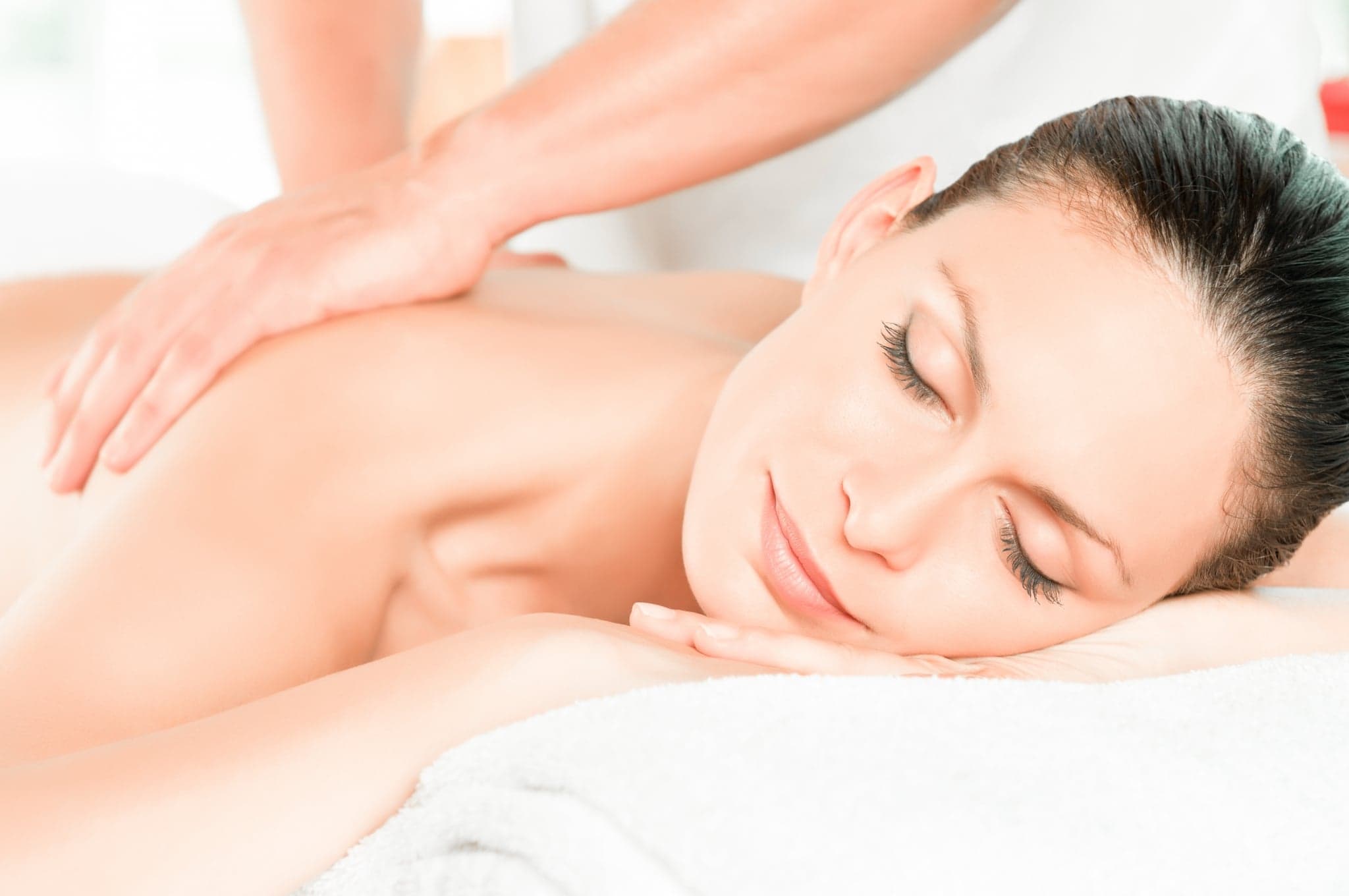 Relaxing Back Massage Spa Treatment Woman relaxing during a back massage on a white towel at a spa.