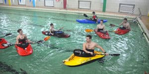 Kayakers practicing in an indoor pool Group of kayakers in colorful kayaks practicing in an indoor pool.