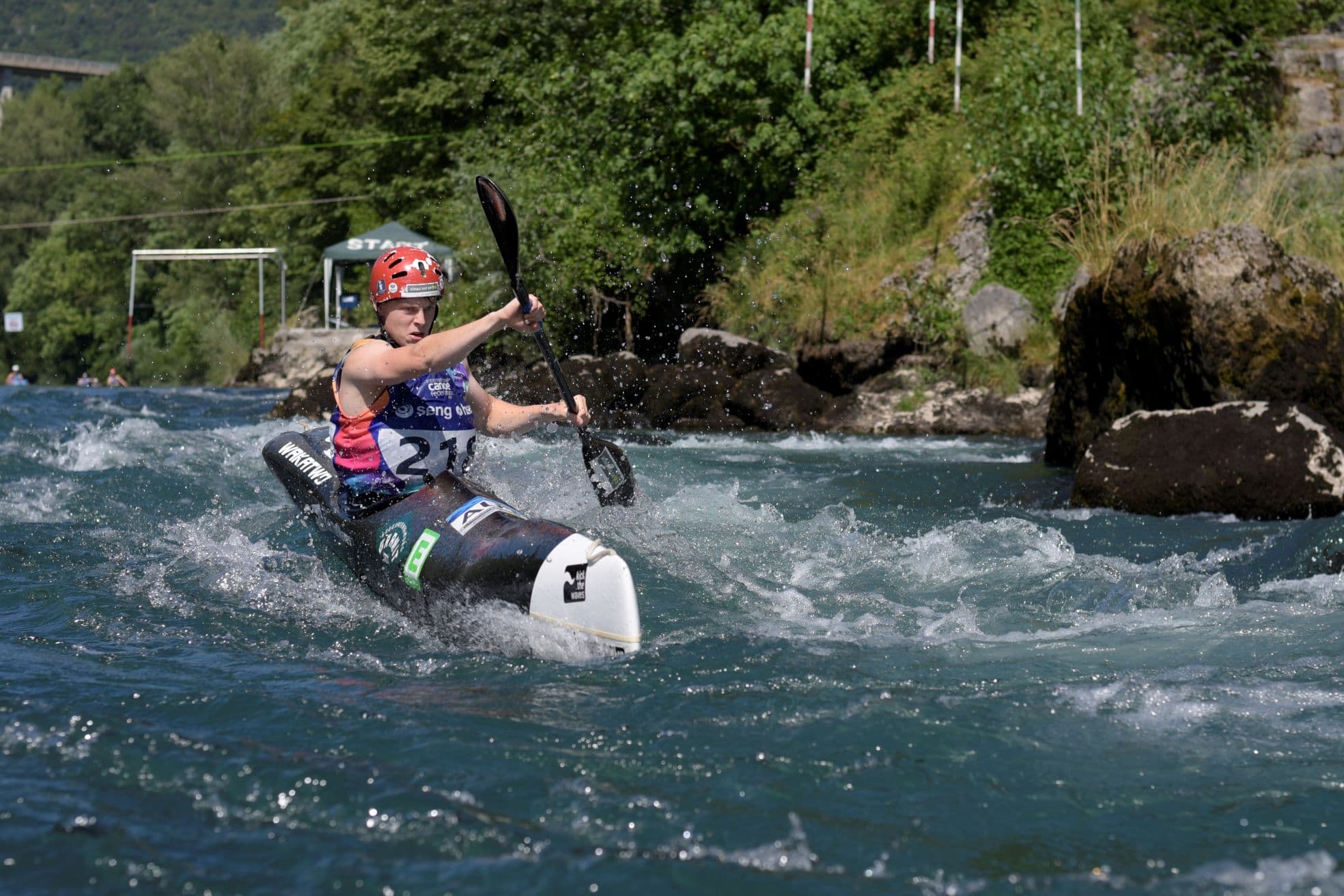Kayaker paddling through whitewater rapids Kayaker wearing a red helmet paddling through churning whitewater rapids.
