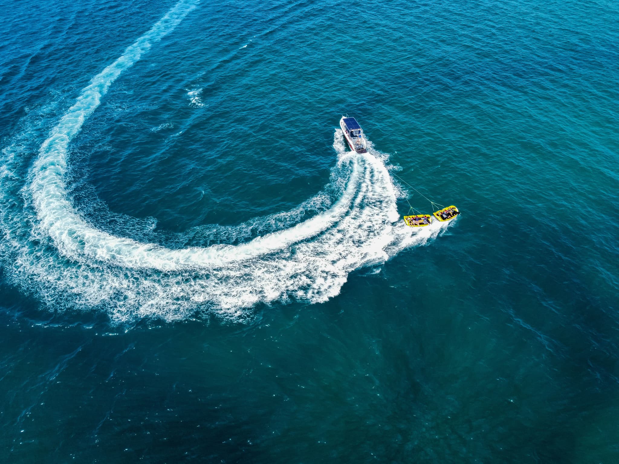 Speedboat Towing Inflatable Tube on Ocean Speedboat towing a yellow inflatable tube across blue ocean water with white wave wake.