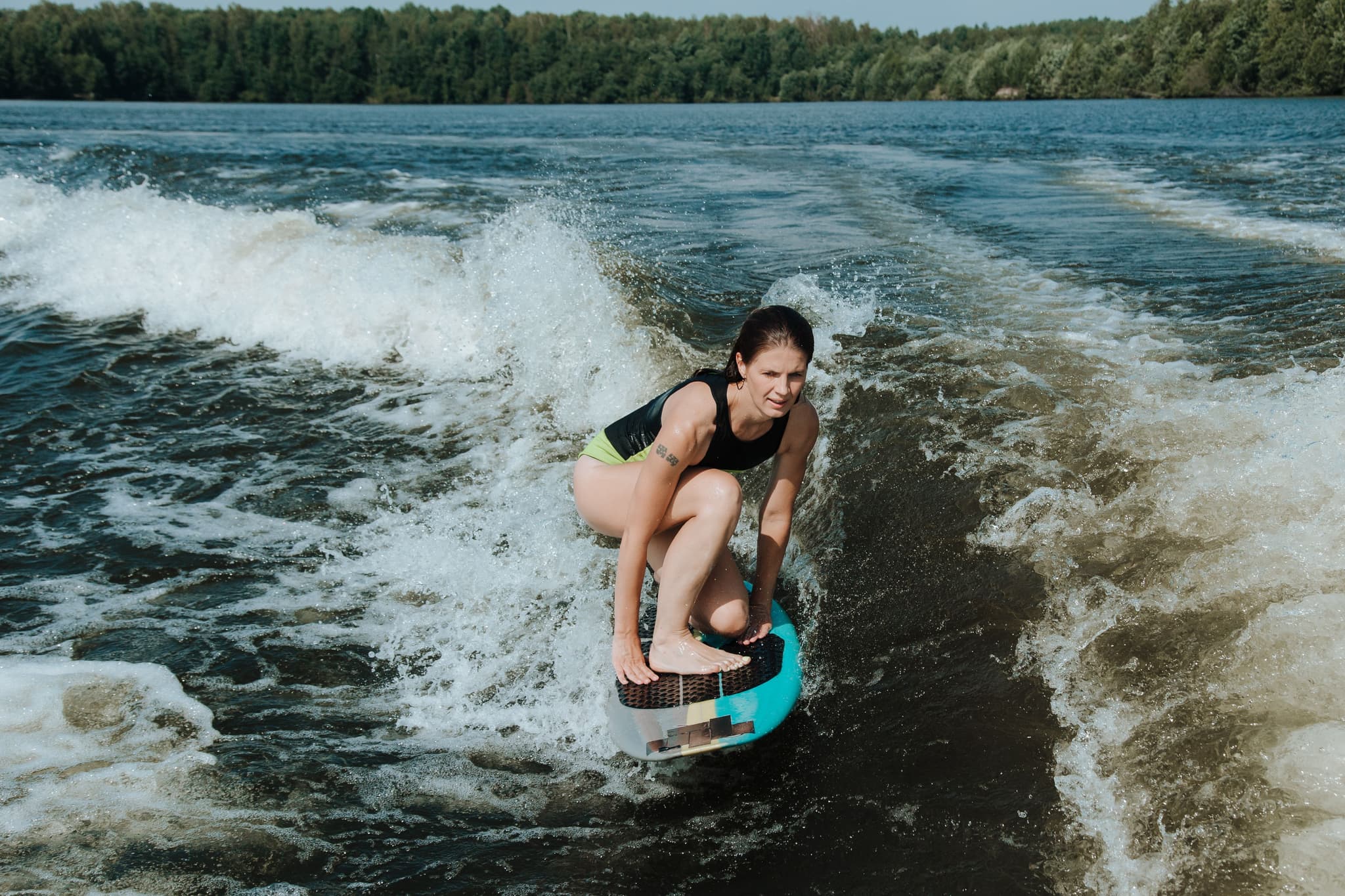 Woman Kiteboarding on Lake With Waves Woman kiteboarding on a lake with waves, wearing a black tank top and neon shorts, holding a blue and black kite board, with a forested shoreline in the background.