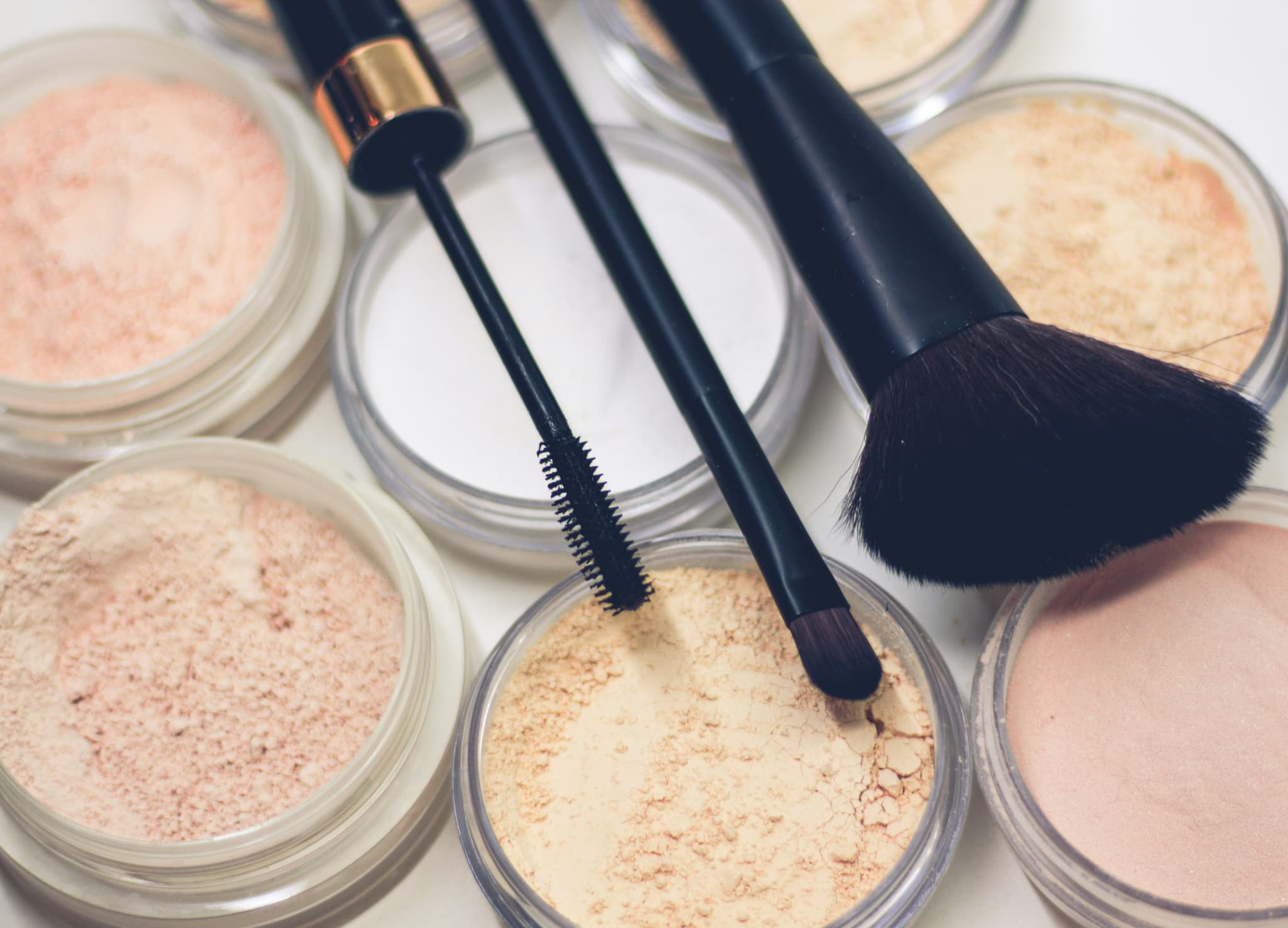 Makeup Brushes and Powder Cosmetics Makeup brushes and loose powder cosmetics in clear containers arranged on a white surface.