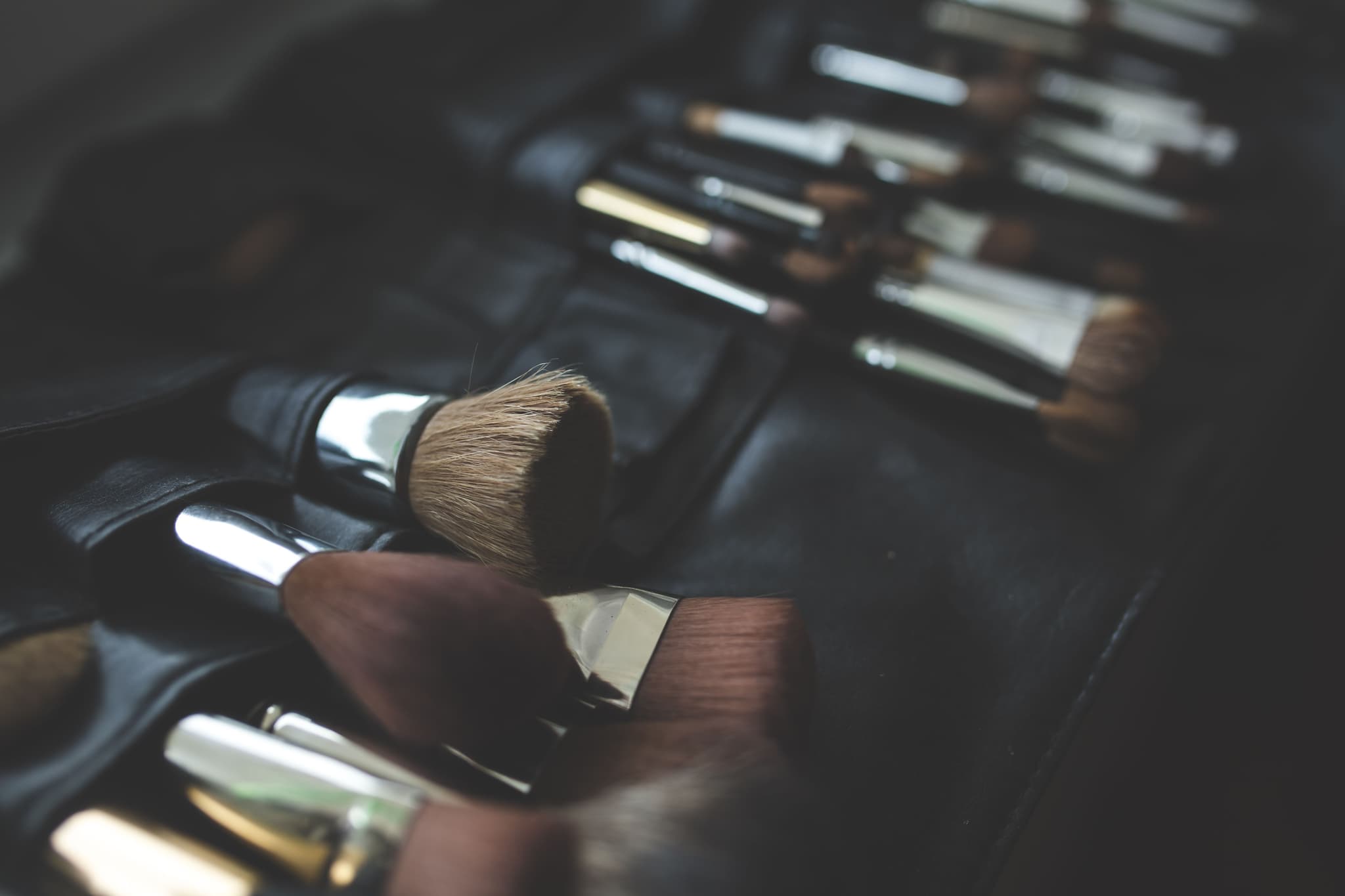 Makeup Brushes With Wooden Handles Collection of makeup brushes with wooden handles and metal ferrules arranged on a dark surface.