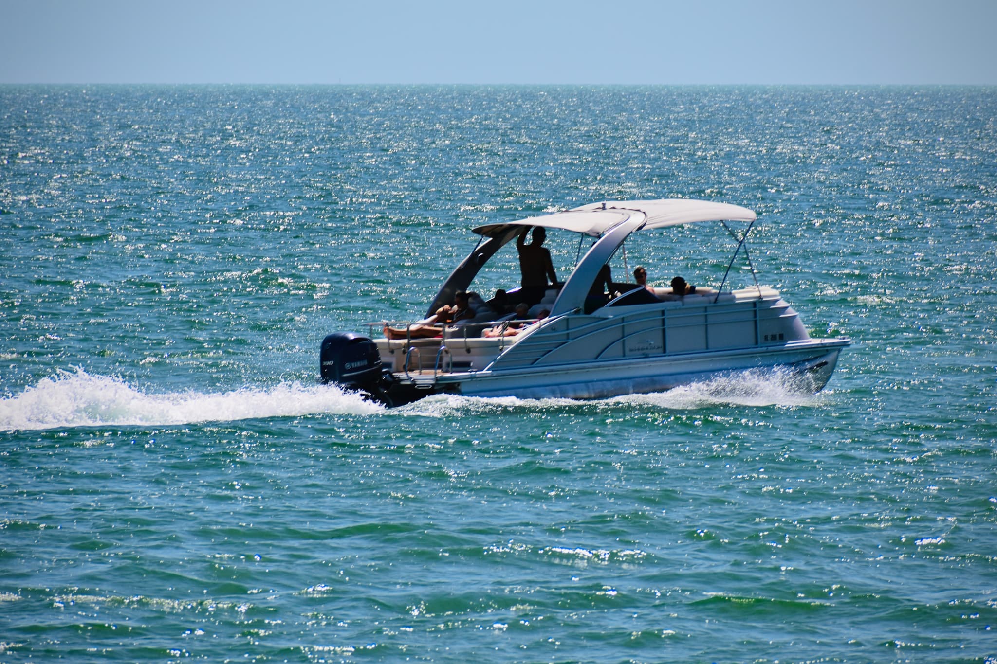 Pontoon Boat in Shallow Ocean Water Pontoon boat with passengers in shallow ocean water with waves and blue sea in background.