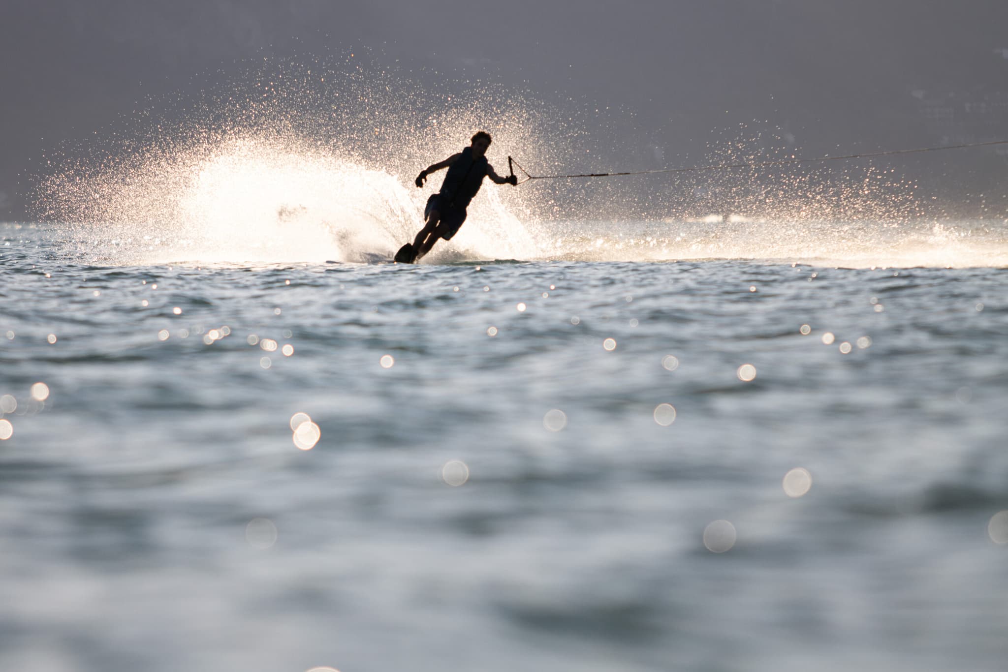 Wakeboarder im Ozeanspritzwasser Silhouette eines Wakeboarders, der durch das Wasser schneidet, mit dramatischem Spritzwasser und Gegenlicht.