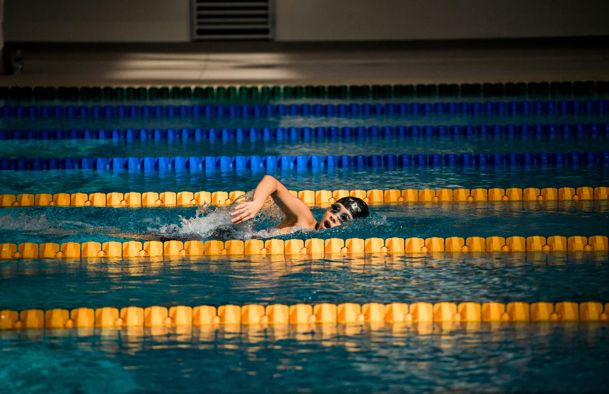 Swimmer Racing in Competition Pool Swimmer performing freestyle stroke in an indoor competition pool with yellow and blue lane dividers.