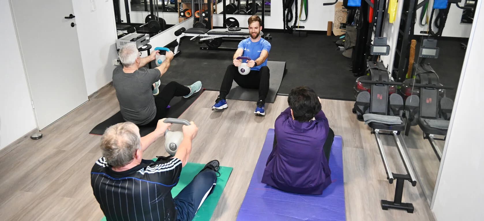 Group Kettlebell Exercise in Gym People sitting on mats doing kettlebell exercises in a gym.