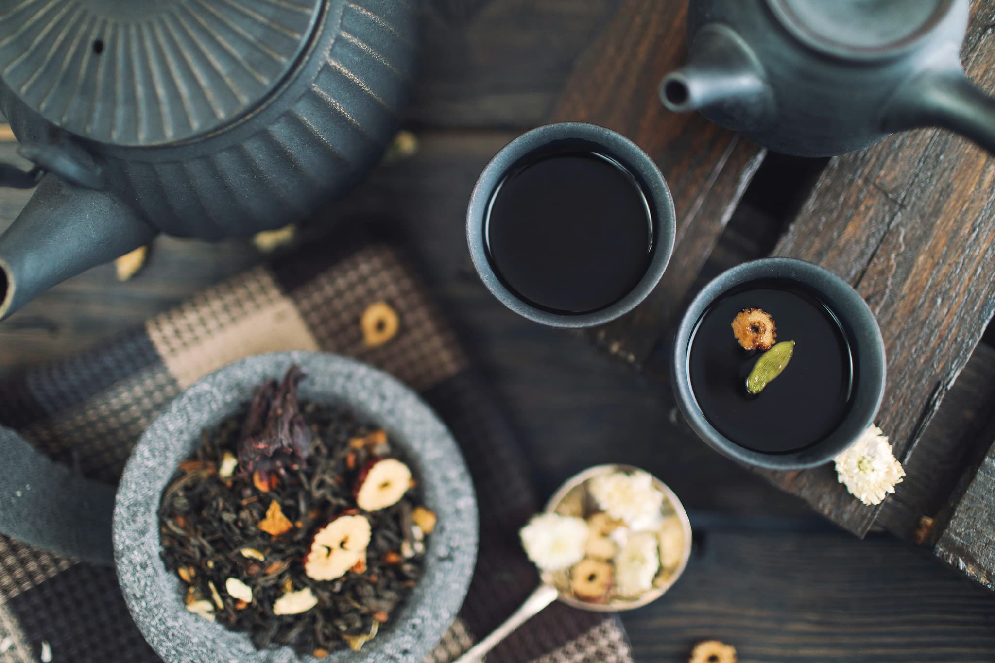 Loose Leaf Tea and Brewed Cups Loose leaf tea with dried flowers and nuts in a gray bowl, two cups of dark brewed tea, and a teapot
