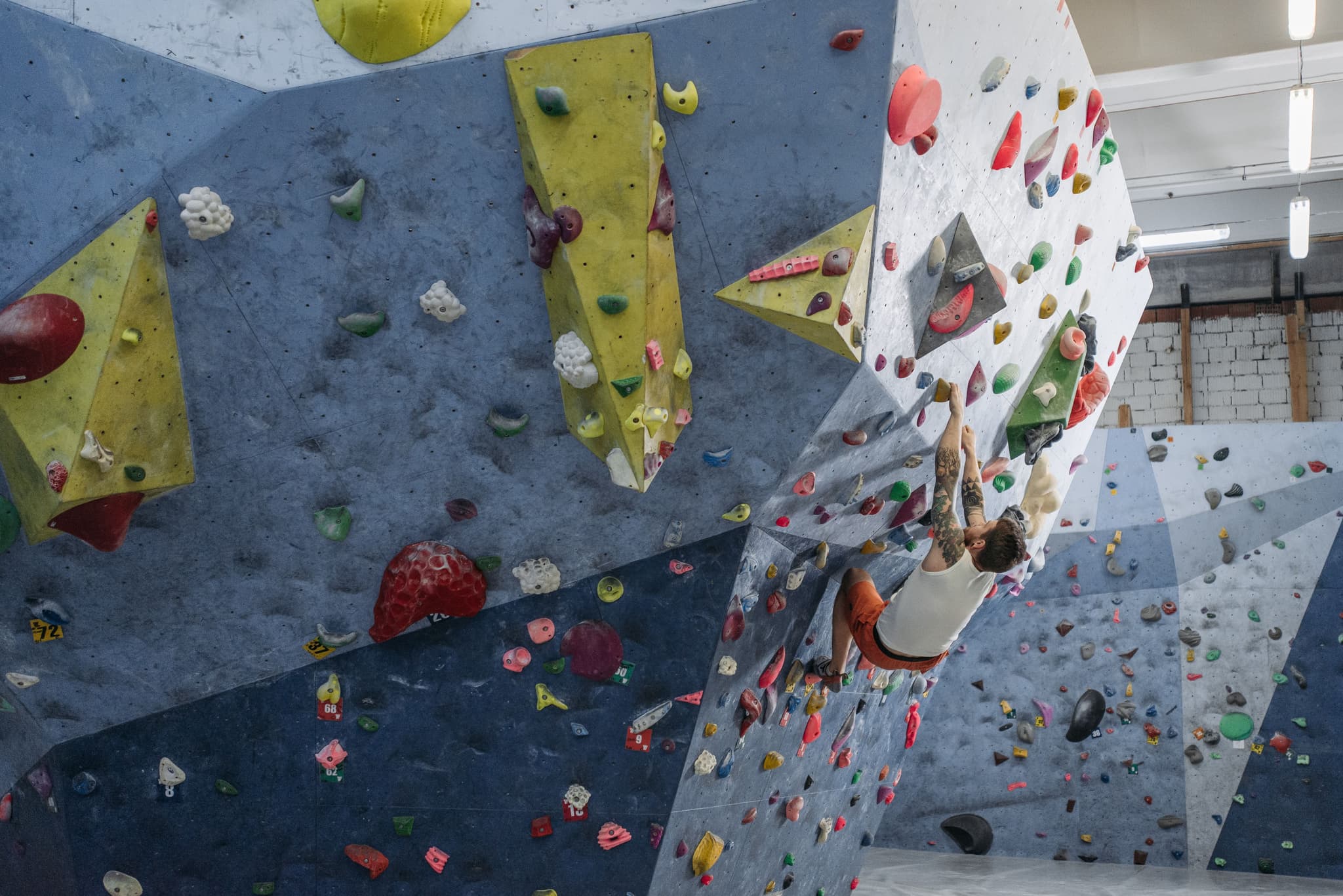 Indoor Climbing Wall with Colorful Holds Person climbing an indoor rock wall with colorful holds in shades of red, yellow, green, and blue.