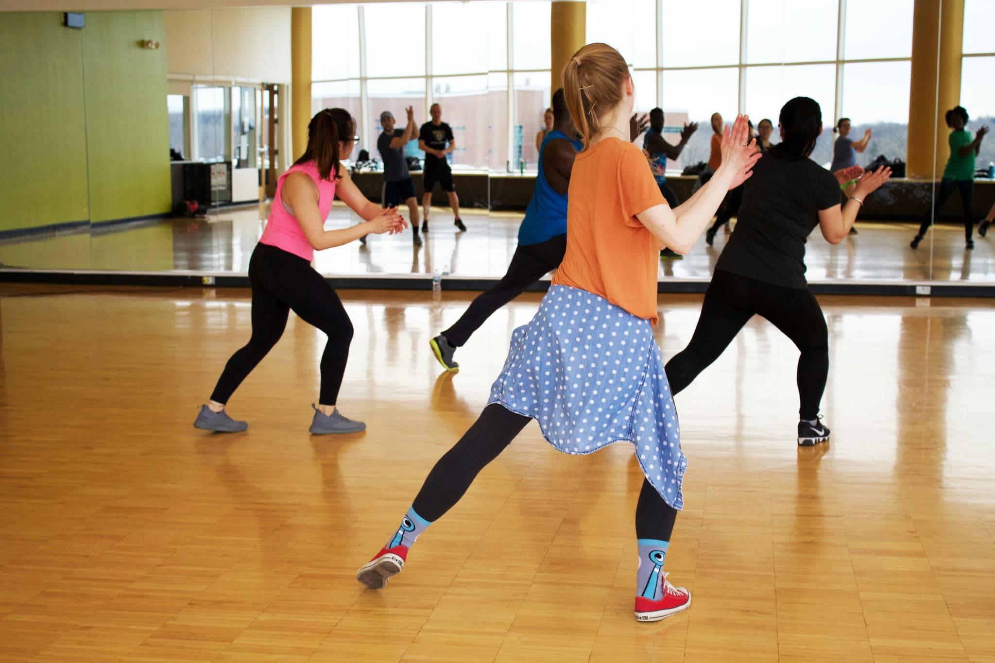 Group Fitness Dance Cardio Class A group of people participating in a dance cardio fitness class in a bright studio with mirrors and large windows.
