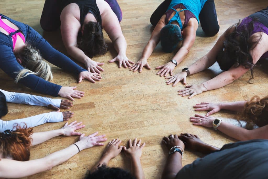 Group Hands Circle Team Activity Multiple people with hands joined together in a circle on a wooden floor during a group activity.