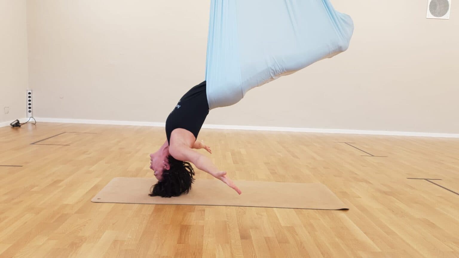 Headstand Yoga Pose in Studio Person performing a headstand yoga pose on a mat in a bright studio with wooden flooring.