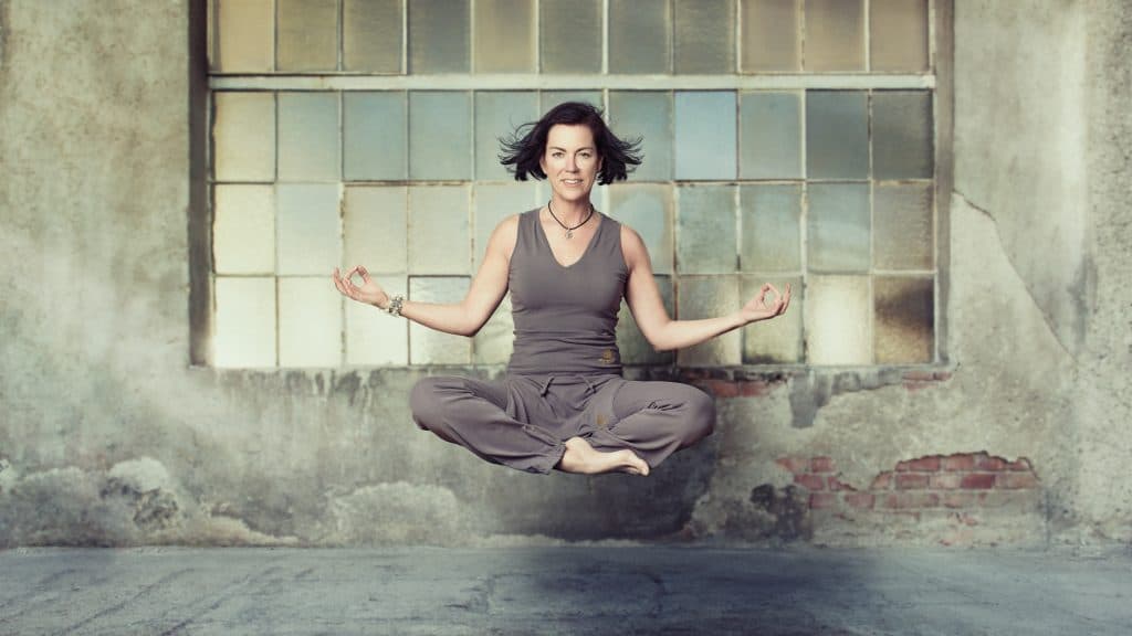 Meditation in Industrial Space Person in meditation pose sitting cross-legged in front of a large industrial window with a weathered concrete wall.