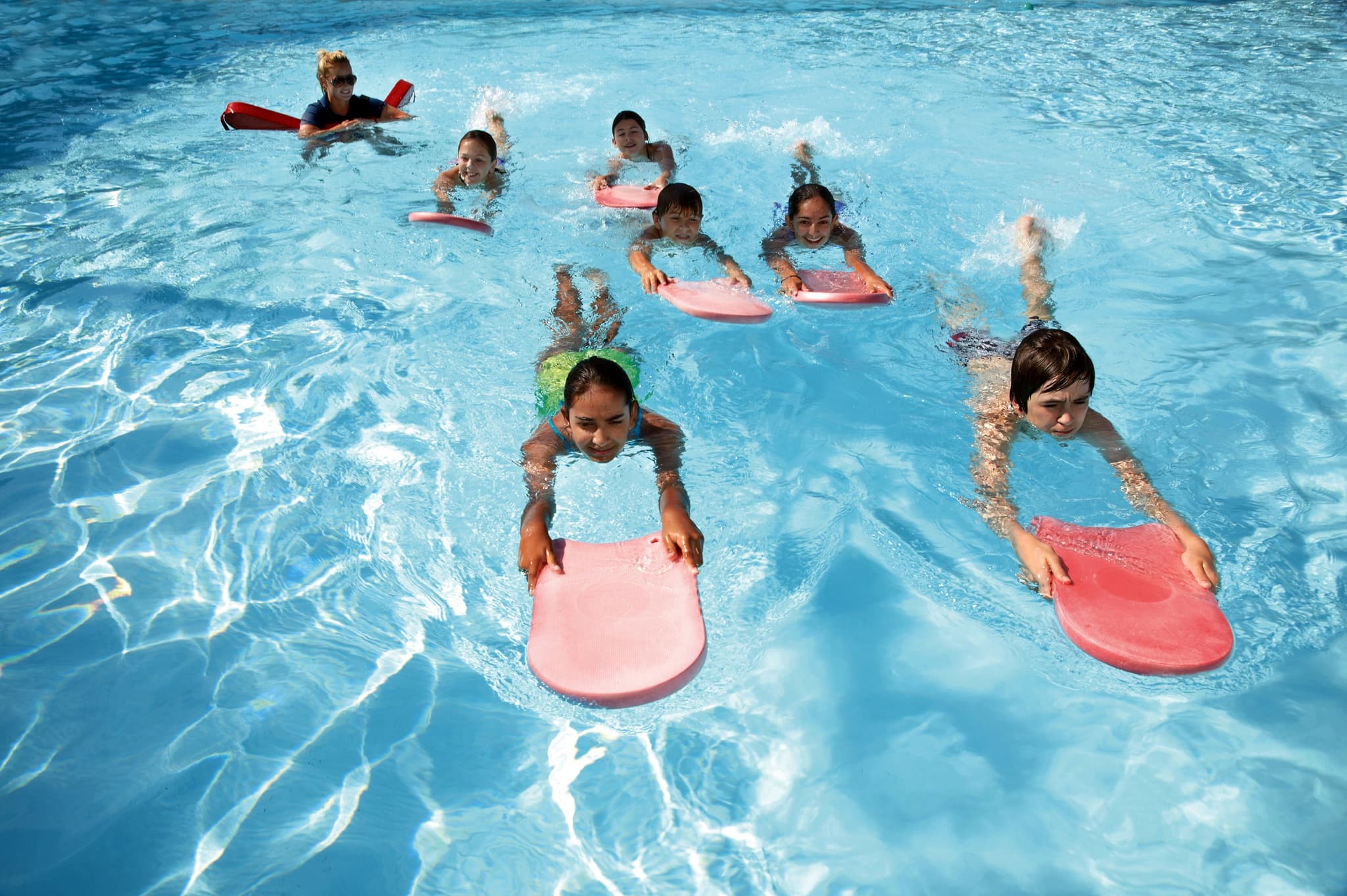 Schwimmkurs für Kinder Kinder beim Schwimmunterricht in einem hellen blauen Becken, mit rosa und roten Kickboards.