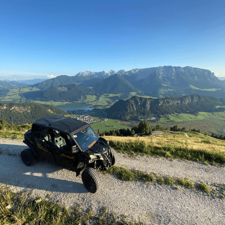 Off-Road Buggy on the Alpine Ridge Off-road buggy parked on a gravel ridge overlooking a green alpine valley and mountains.