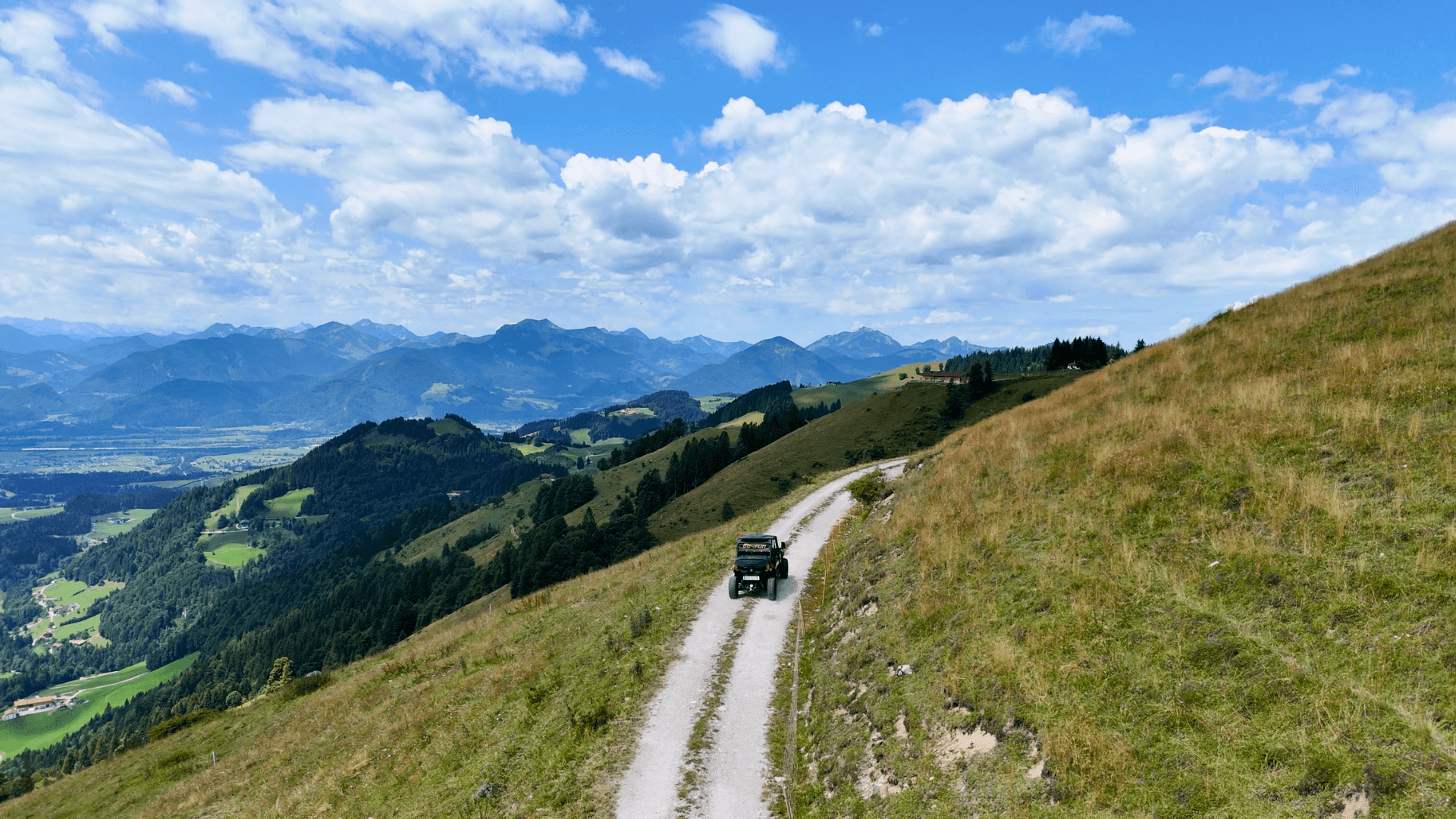 Off-road vehicle on a mountain ridge trail Off-road vehicle on a gravel path in the mountains with a view of a green alpine valley.