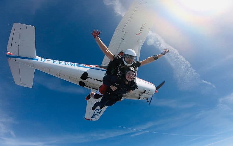 Tandem Skydivers Freefall Above Airplane Tandem skydivers in freefall above a small airplane against a blue sky.