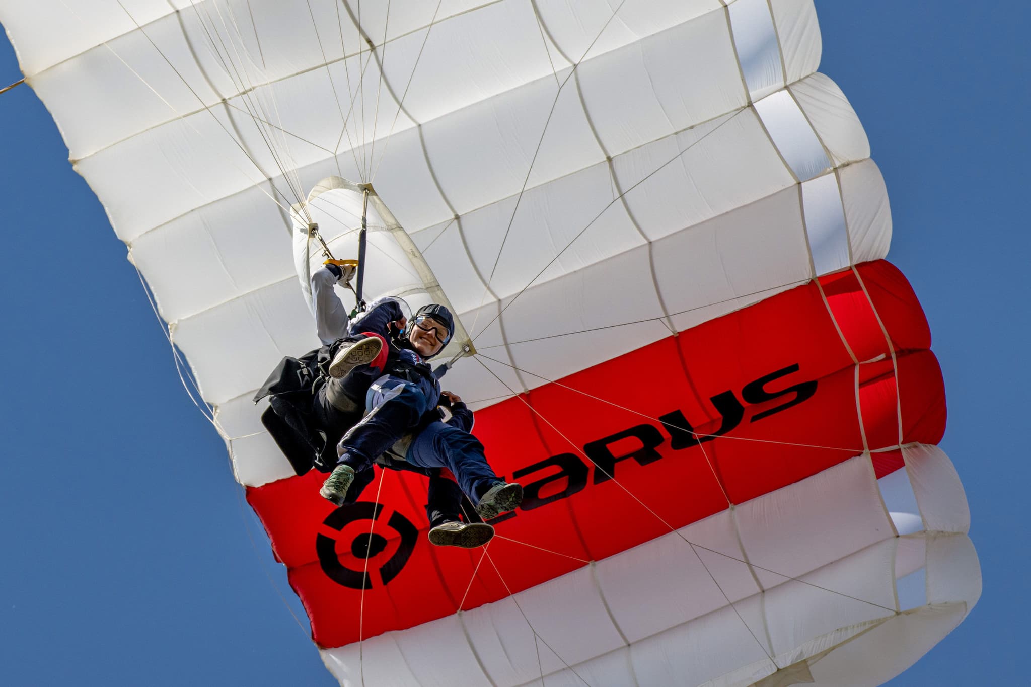Tandem Skydivers Under Open Parachute Two tandem skydivers smiling under an open red and white parachute canopy.