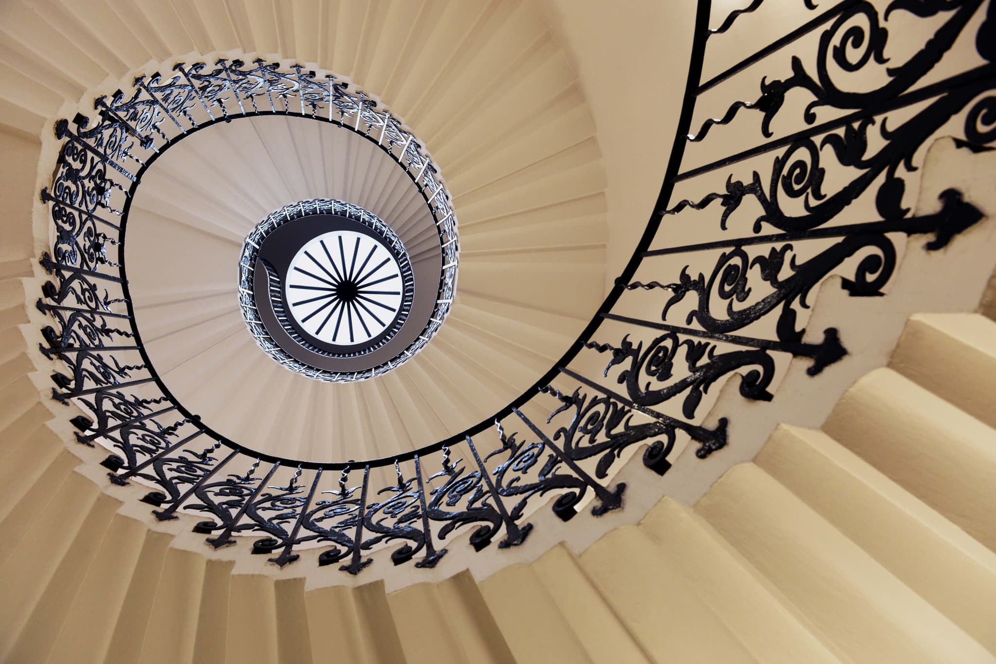 Spiral Staircase With Ornate Iron Railing Overhead view of a spiral staircase with ornate black iron railings and cream-colored steps spiraling downward.